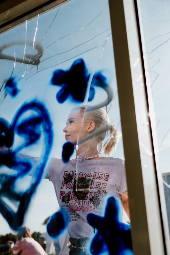 A creative artist painting blue graffiti on a window with vibrant colors in an urban setting.